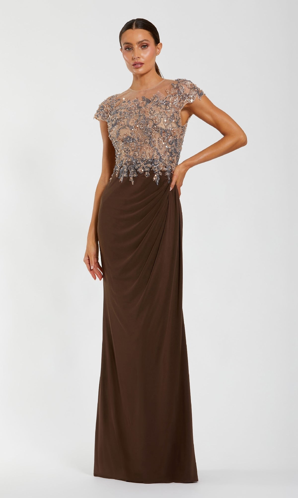 A woman poses against a white background in the Mac Duggal 21100 Beaded-Bodice Long Formal Dress, featuring a chocolate brown floor-length skirt and sheer embellished cap-sleeve bodice.